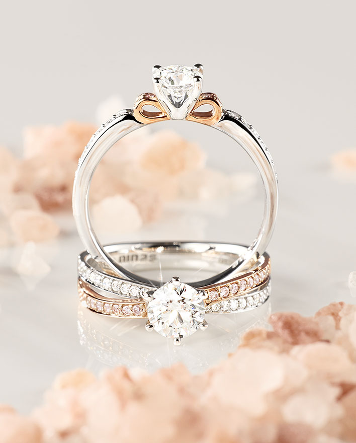 Two white diamond engagement rings with pink diamond accents surrounded by pink rock-salt texture